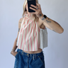 Person wearing a red-striped halter top and blue jeans, taking a mirror selfie.