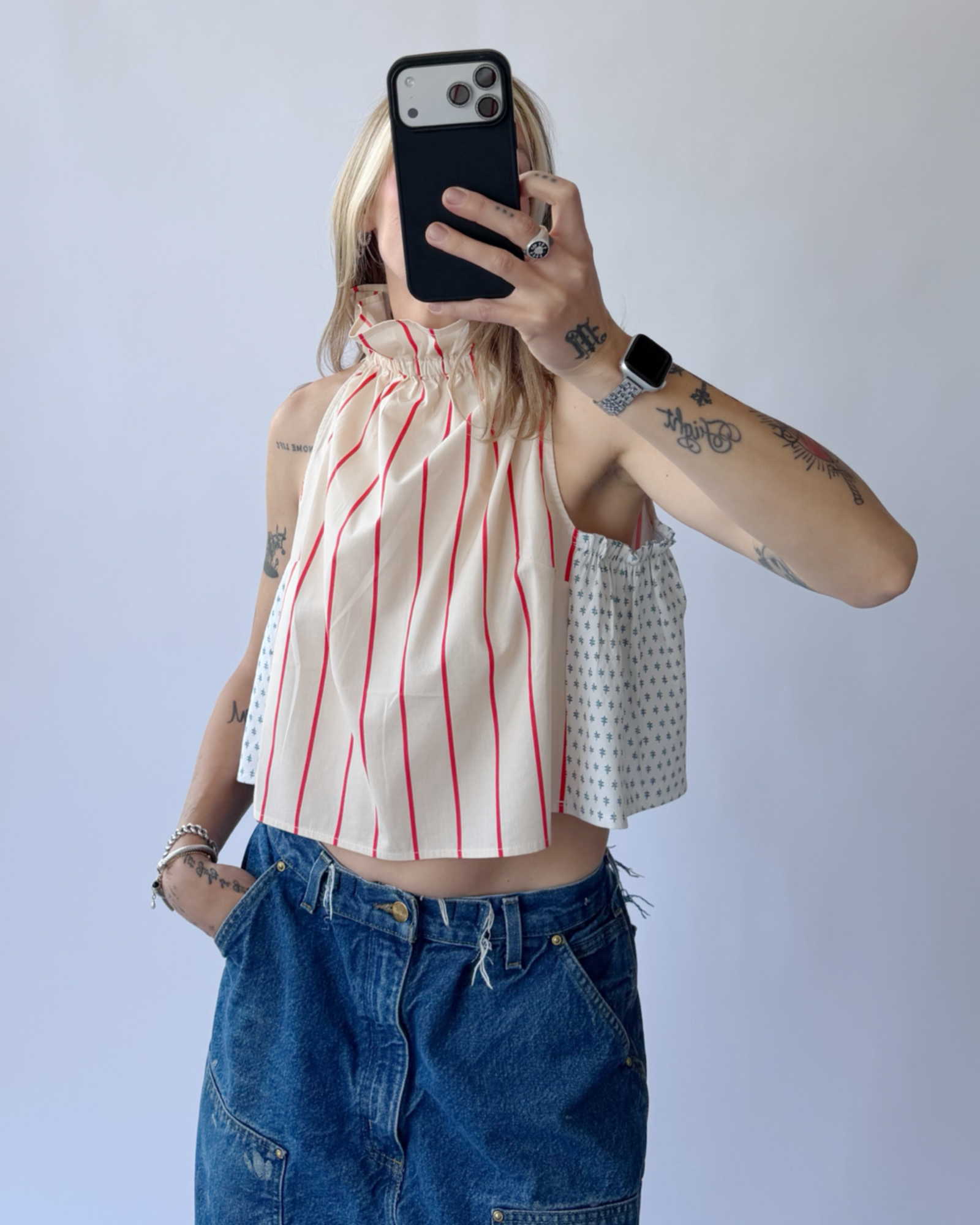 Person wearing a red-striped halter top and blue jeans, taking a mirror selfie.