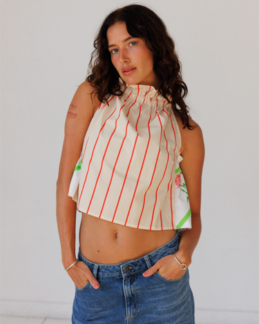 Woman wearing a sleeveless striped top with floral details and blue jeans against a plain background