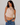Woman wearing a sleeveless striped top with floral details and blue jeans against a plain background
