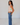 Woman wearing a sleeveless striped top with floral details and blue jeans against a plain background