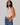 Woman wearing a sleeveless striped top with floral details and blue jeans against a plain background