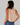 Woman wearing a sleeveless striped top with floral details and blue jeans against a plain background