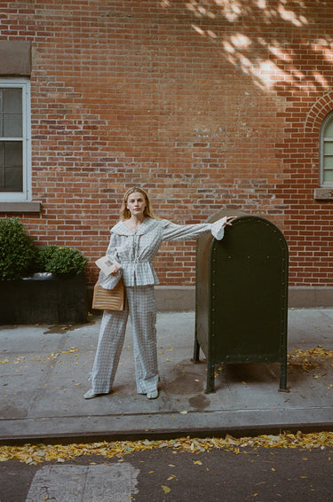 A woman standing outside in front of a mailbox wearing a blue plaid top with a sailor-style collar and matching pants with an elasticated waistband and cuffed hems. The outfit features drawstrings and is tied at the front.