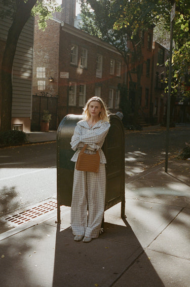 A woman standing outside in front of a mailbox wearing a blue plaid top with a sailor-style collar and matching pants with an elasticated waistband and cuffed hems. The outfit features drawstrings and is tied at the front.