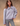Woman wearing a light blue wool jacket and light wash jeans against a tan fabric backdrop.