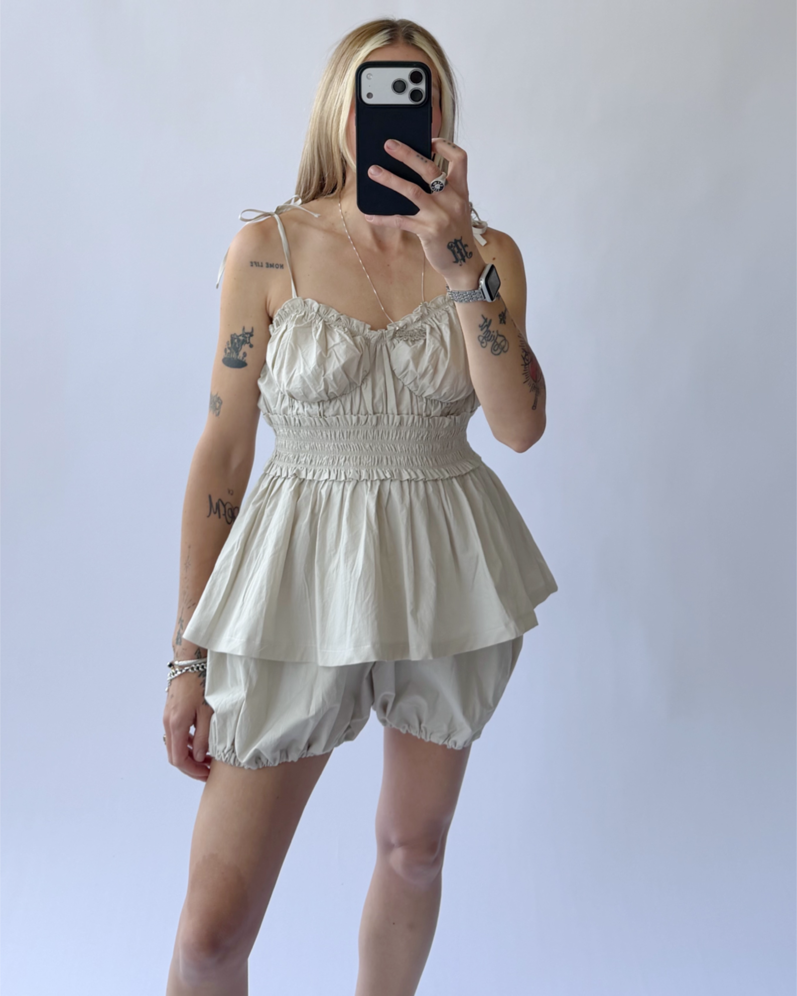 Person wearing a light-colored sleeveless top and shorts against a plain background