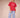 Woman wearing a red t-shirt and blue stripe casual pants with ruffled ankle hem on a plain background.
