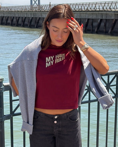 Woman wearing a red crop top with text and dark jeans by a waterfront.
