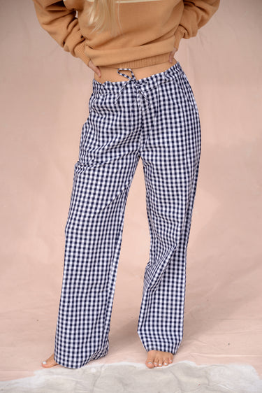 Woman wearing a tan sweater with navy blue and white gingham pants on a beige background.