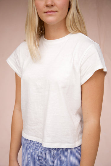 Woman wearing a white t-shirt and blue striped pants against a pink background
