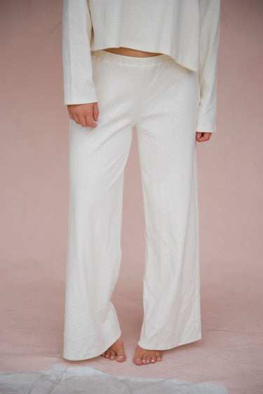 Close-up of woman wearing cream pointelle pants against a pink background.