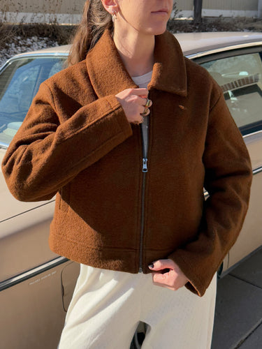 Woman standing in front of a vintage car outdoors zipping up a brown wool jacket.