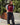 Person wearing a red shirt with text and black pants standing outdoors.
