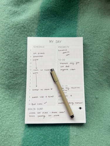 Notepad with a daily schedule and pen on a green fabric background