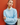 A woman wearing a light blue crewneck sweater over a white high-neck collared shirt, standing against a textured red-orange wall.