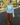 A woman walking outdoors on a paved street wearing a light blue crewneck sweatshirt and brown wide-leg pants, holding a paper coffee cup.