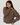 A woman wearing a brown and white horizontally striped long-sleeve knit top, paired with white pants, photographed against a plain light gray studio background.