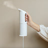 Hand holding a white handheld steamer against a beige background