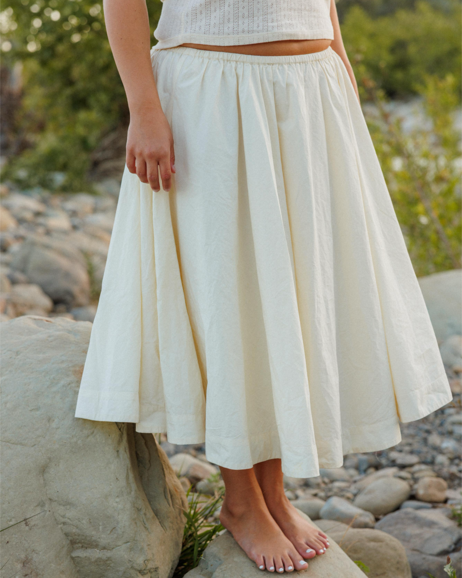 Person wearing a cream skirt standing on rocks with a natural background
