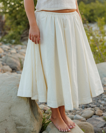 Person wearing a cream skirt standing on rocks with a natural background
