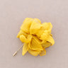 A yellow fabric flower brooch with a gold-tone pin, displayed on a neutral gray background.