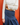 A person wearing a cream draped long-sleeve top and a dark blue pleated skirt, standing against a solid orange-red wall.
