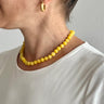 Person wearing a yellow beaded necklace and gold hoop earrings against a plain background