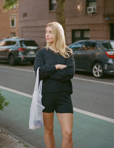 Woman standing outside in an urban setting wearing a black knit sweater with matching knit shorts.